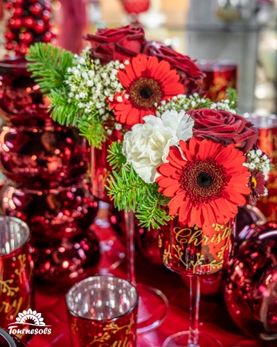 Bouquet de fleurs rouges et blanches dans un verre décoré de Noël.
